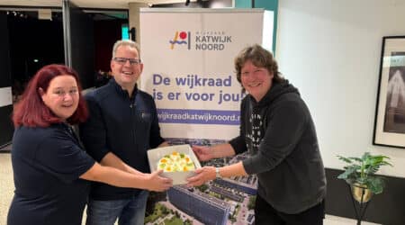 Een communitylid krijgt een taart overhandigd van wijkraad Katwijk Noord